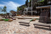 Two wooden benches . Two tall triangular shaped wooden structures resembling tents. shades and stepping stones in the background. 
