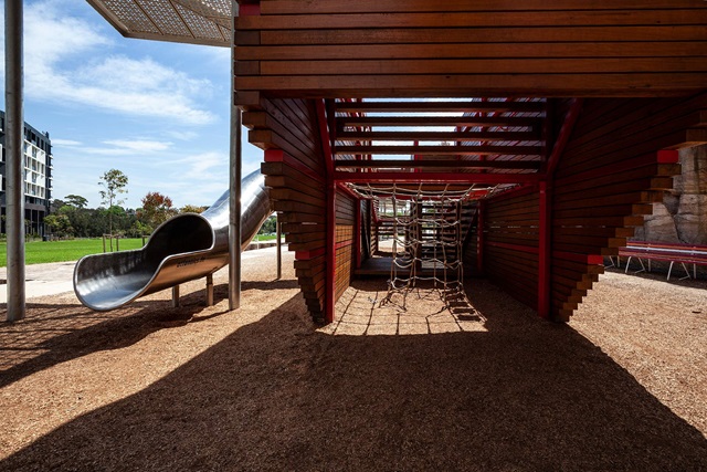 detail of wooden enclosed playground sculpture with attached tube slide and scramble, climbing net.