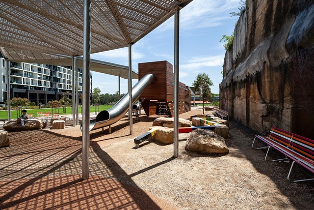 Steel shade structure and enclosed steel tube slide attached to a wooden enclosed playground sculpture.