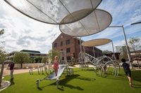 Children on play equipment and large circular shade structures over the playground