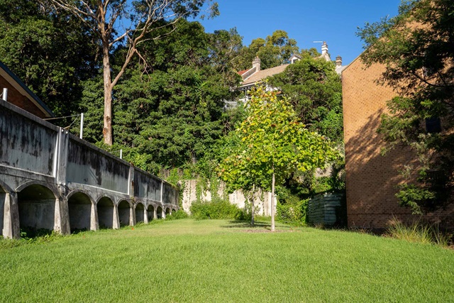 A lawn with some young trees. An aqueduct runs along the length of the lawn to the left side.