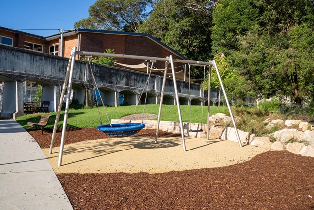 Swing set in the reserve featuring one seat-style swing and one basket-style swing. Near it is a wooden bench.