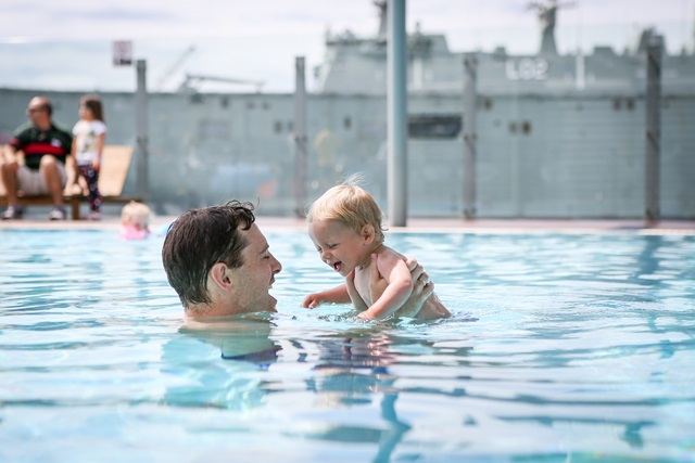 A father holds his young child above the water in the pool
