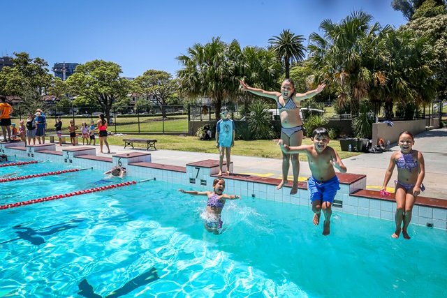 A group of young children jumping into the 50 metre outdoor pool.