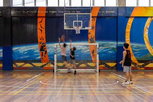 Children playing a basketball court with a mural in the background
