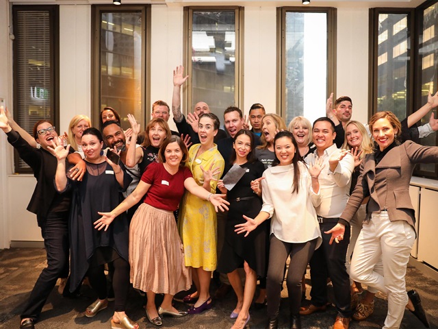 Cheerful group of people standing together and some throwing their arms into the air.
