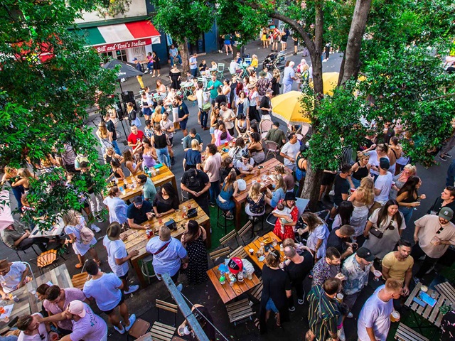 Aerial view of dozens of people enjoying food, drink and entertainment on a road