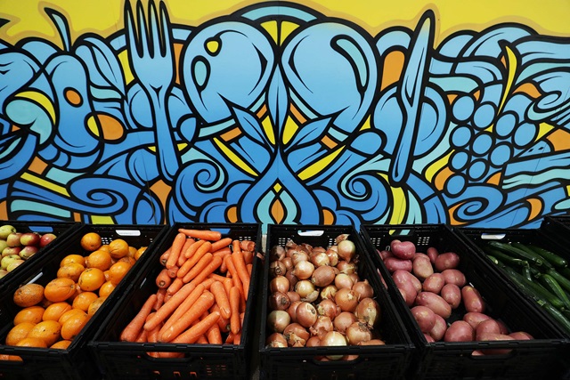 apples, oranges, carrots, onions, potatoes and zucchinis in black plastic crates lined up against colourful wall at OzHarvest's Waterloo market.