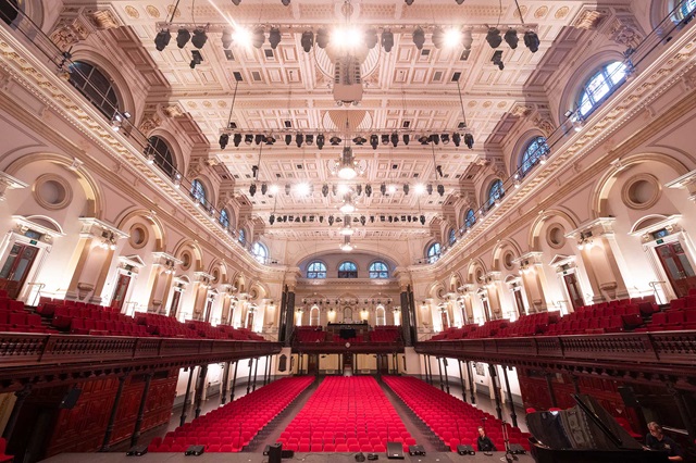stage view of empty main hall in Sydney Town Hall with two levels of red seat rows.