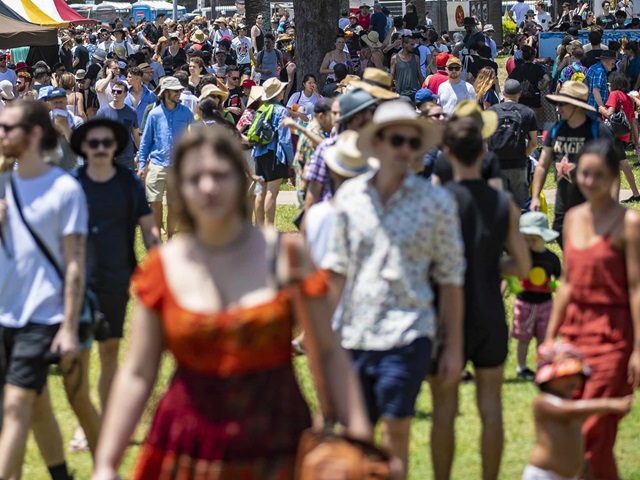 A crowd of people walking through a festival ground on a sunny day