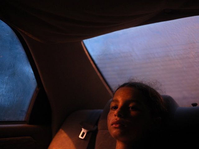 A young girl sitting in the back seat of a car on a rainy night