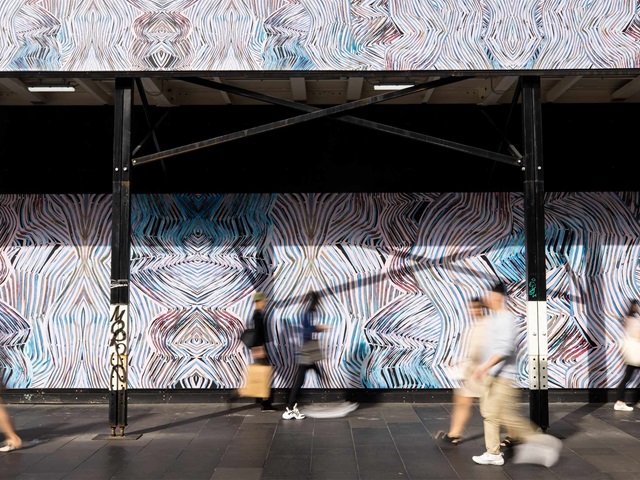 Handful of motion blurred people walking past hoarding and scaffolding in Sydney's CBD.