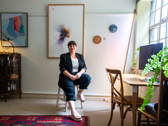 An adult sitting on a chair in their artist studio