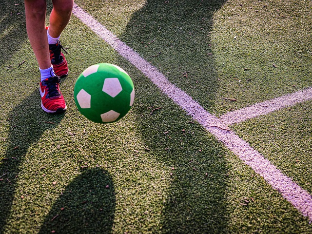 A close-up of a soccer ball just before it hits the ground in front of a child's feet.