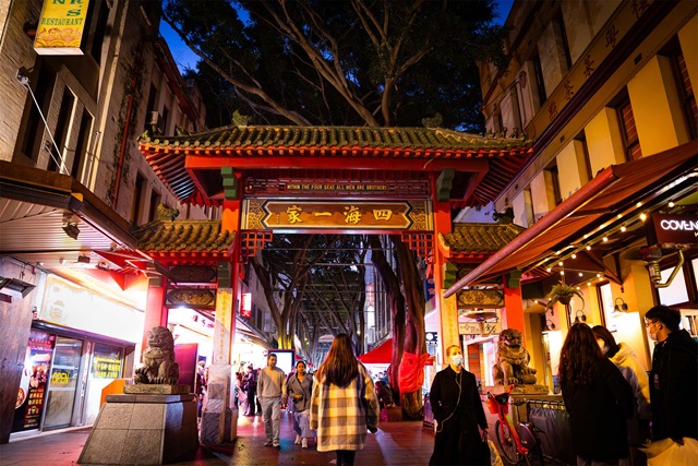 People walking along Dixon Street, Chinatown, Sydney at night and passing through the large decorative gate there.