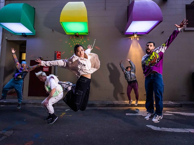 Five dancers strike a pose. They're on a city laneway, lit by colourful lights. Credit: Wanna Dance, City People/Anna Kurcera