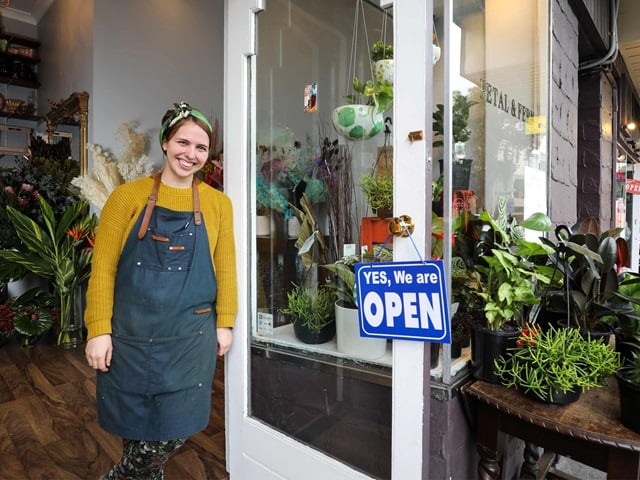 Woman standing outside a florist shop surrounded by flowers