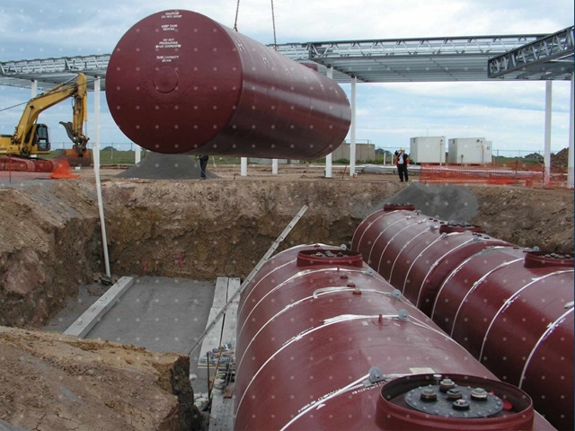 A petroleum tank held in the air by a crane being placed in to the ground next to another two tanks.