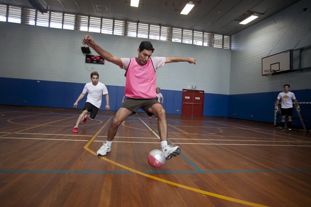 2 adults playing soccer on an indoor court.