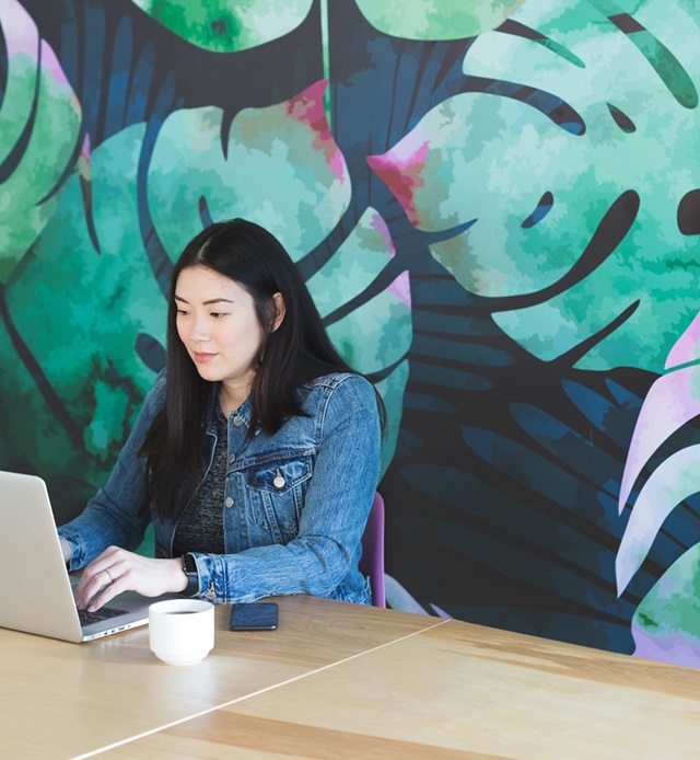 Woman sitting at laptop in front of colourful wall