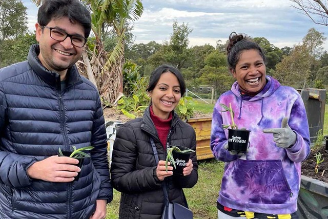 Three volunteers in a community garden smiling at the camera and holding one seedling pot each.