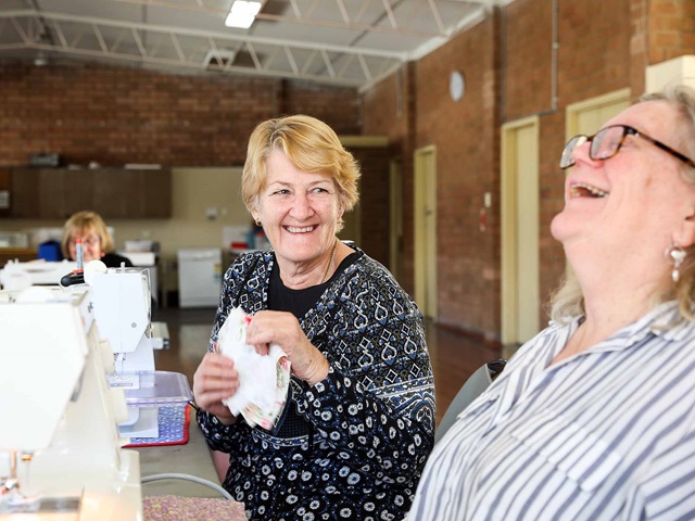 Two women volunteers smile and laugh as they work in a community hall.