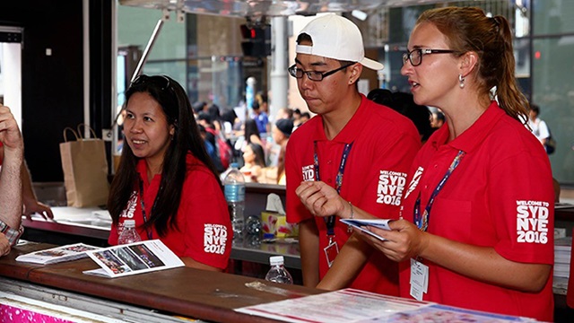 A volunteer helps a visitor with directions besides a way finding map