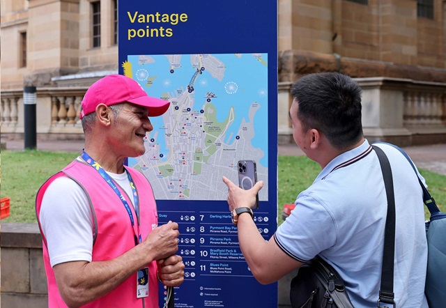 A volunteer helps a visitor with directions besides a way finding map