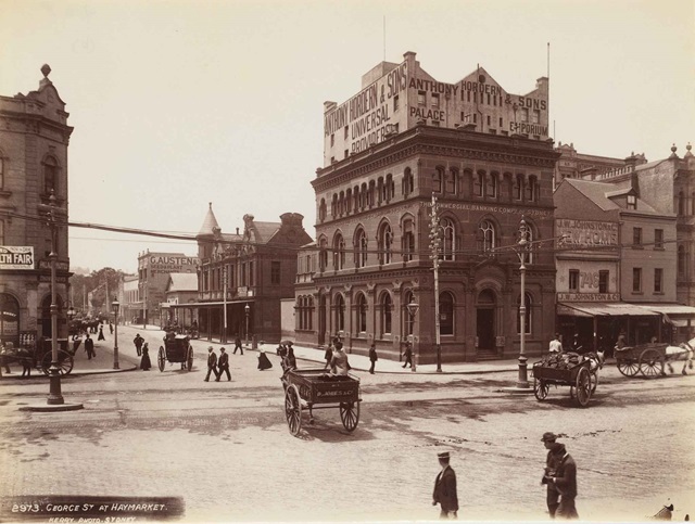 An historical image of a street corner with brick heritage buildings, horse-drawn carts and pedestrians in suits and hats.
