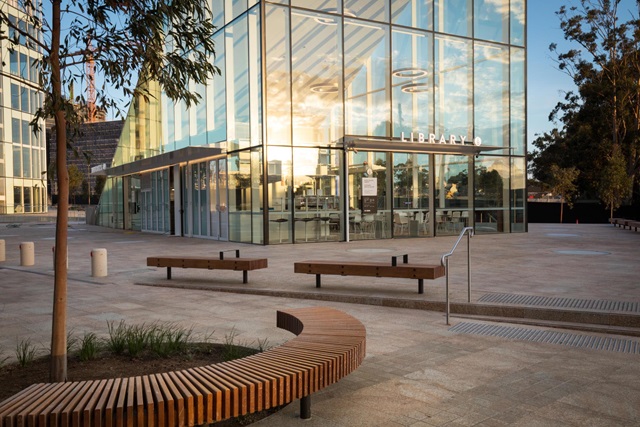 Bench and tree in foreground, seating in the middle and glass building that is the library in the distance