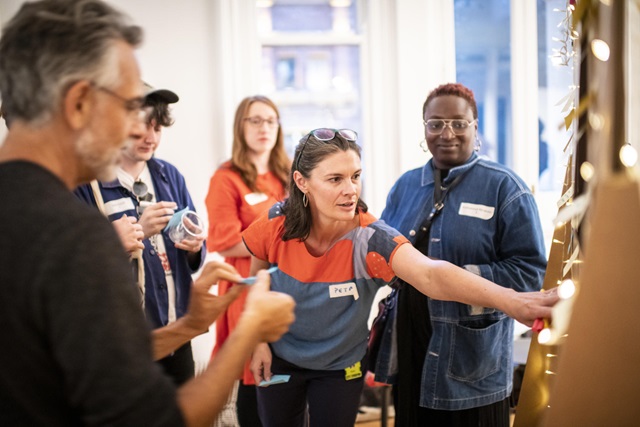 A woman points to a consultation board while others watch.