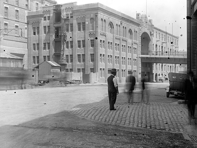 Black and white image of 4 men standing outside Hickson Road Bond Stores with other large buildings in the background.