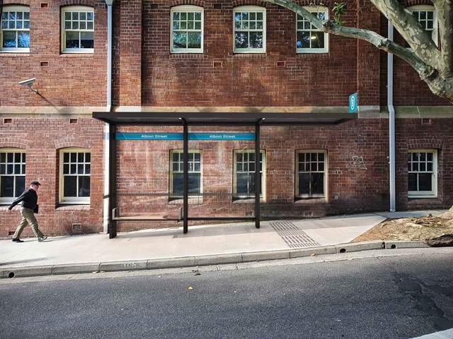 A man walks towards a bus shelter on a city street pavement.