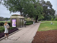 A city park. Beside the pavement is a toilet with a digital screen on its side wall.