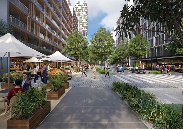 View along a street with ample sidewalks flanked by apartment buildings. There is an outdoor cafe seating.