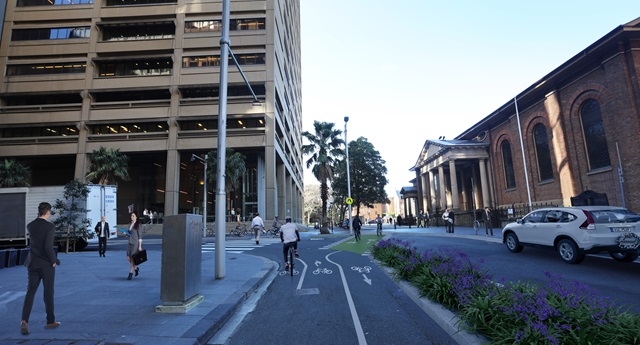 People walk on the footpath while people ride bikes on the proposed separated cycleway, with a garden bed between it and the roadway.