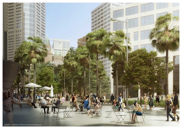 Many people are seated at tables while others walk through the paved area, which is surrounded by trees. 