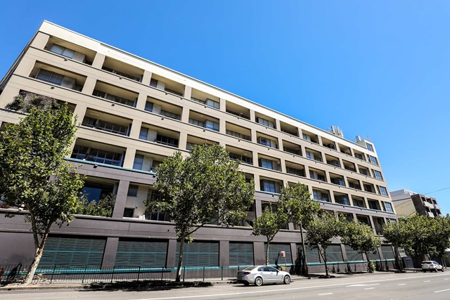 A 6-storey apartment building with inset balconies on a tree-lined city street on a clear day.
