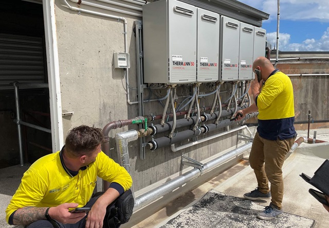two blue-collar workers looking at gas storage water heaters placed on a rooftop.