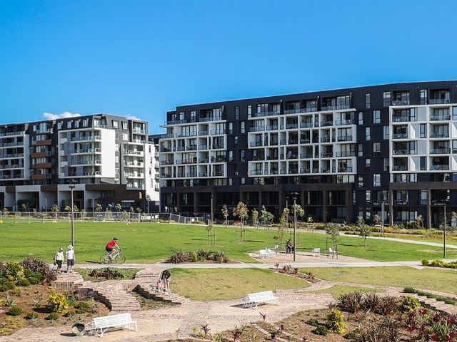 People walk and cycle through parkland adjoining a new housing development.