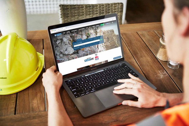 A person browses a website on a laptop. A yellow hardhat is on the table next to the laptop.