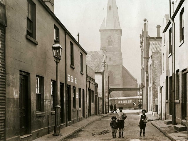 Three small children stand in Valentine Street, Haymarket, 1910.