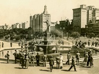 Groups of men and women viewing the fountain in Hyde Park in the 1930s. Trees, avenue and lamps as well as buildings are in the background.