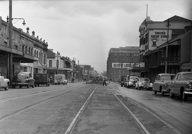 An historic photo of a street with cars and buildings.