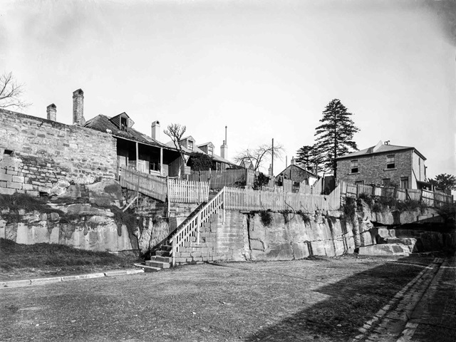 An historic photo of a road and houses up the steps.