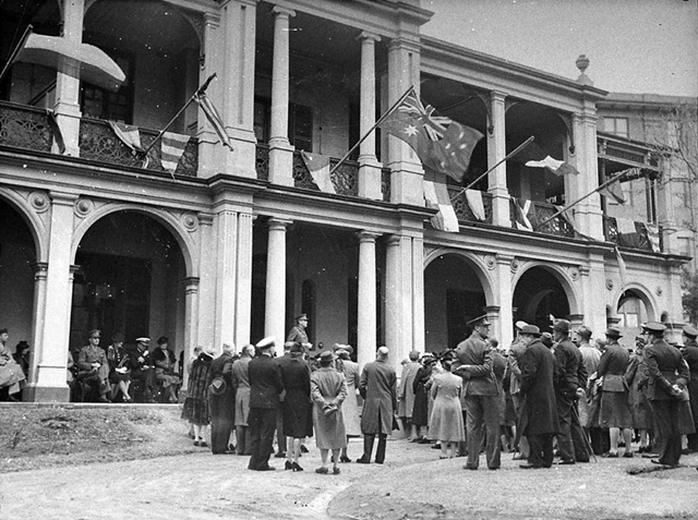An historic photo of people standing in front of a large building.