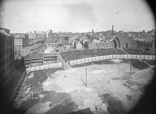 An historic photo of a construction site and buildings in the background.