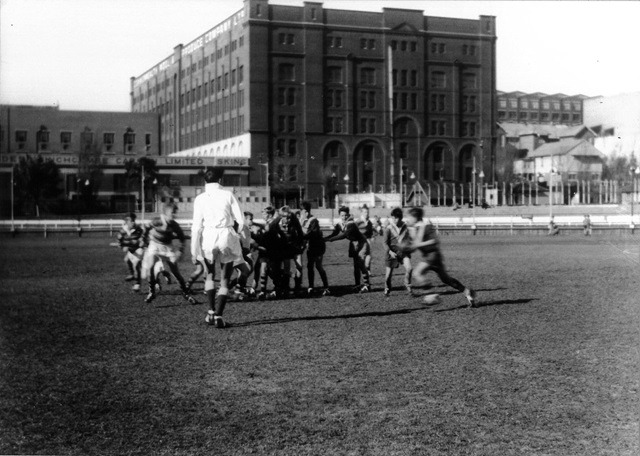 An historic photo of people playing football and a building in the distance.