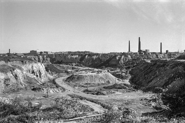 An historic photo of an open area and brick chimneys from a factory in the distance.