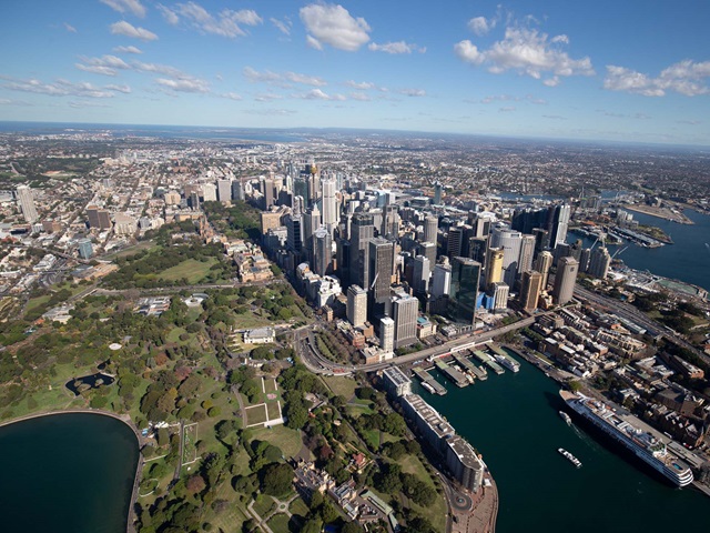 A bird's eye view of Sydney that encompasses the ferry wharves at Circular Quay, tall buildings in the city centre and large areas of parkland at the Royal Botanic Garden.